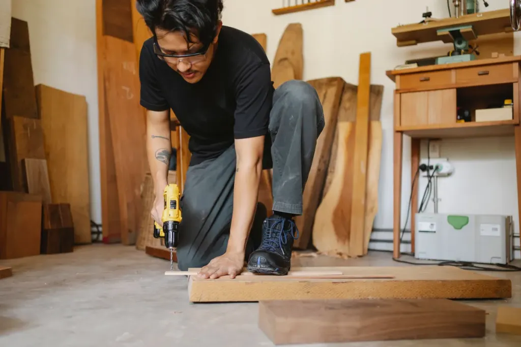Klusser boort een gat in een houten plank in de werkplaats voor een inbouwkast