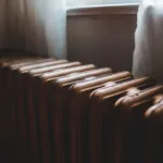 Gietijzeren radiator onder een raam in een lichte kamer, klaar om te ontluchten