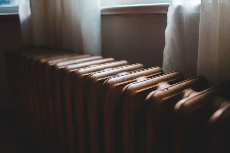 Gietijzeren radiator onder een raam in een lichte kamer, klaar om te ontluchten