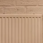 Strakke witte radiator tegen een bakstenen muur, ideaal om een radiatorombouw voor te maken