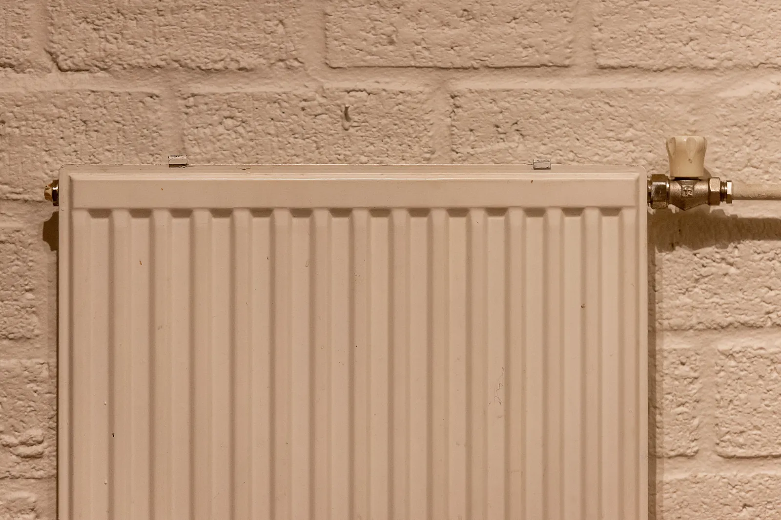 Strakke witte radiator tegen een bakstenen muur, ideaal om een radiatorombouw voor te maken