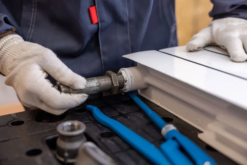 Close-up van handen met gereedschap bij de leiding en kraan van een radiator